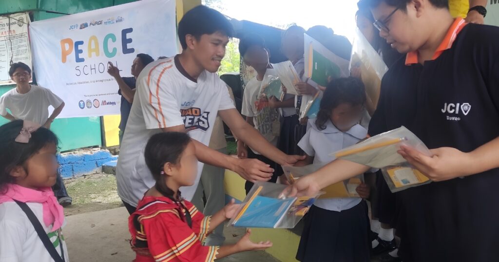 Volunteers distributing notebooks, pencils, crayons, and learning kits to Indigenous learners during P.E.A.C.E. School.